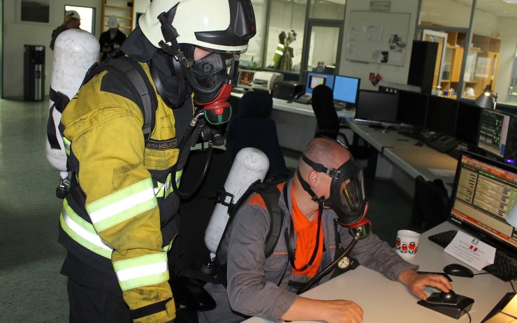 V centrální dozorně zůstal pouze jeden pracovník obsluhy vybavený dýchacím přístrojem s maskou, aby monitoroval situaci v provoze na obrazovkách. Jeho jediným úkolem přitom bylo, zmáčknout příslušné tlačítko pro bezpečné odstavení provozu elektrárny kdyby došlo k nejhoršímu. Dohlížel na něj jeden z hasičů, rovněž s nasazenou dýchací technikou.  Foto: Ota Schnepp / ČEZ